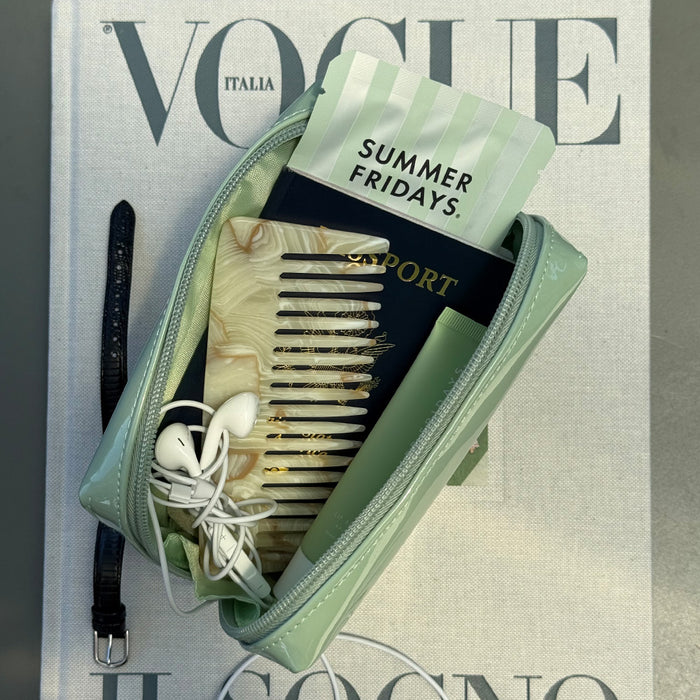 Green travel case with comb, passport, and earbuds on a Vogue magazine cover