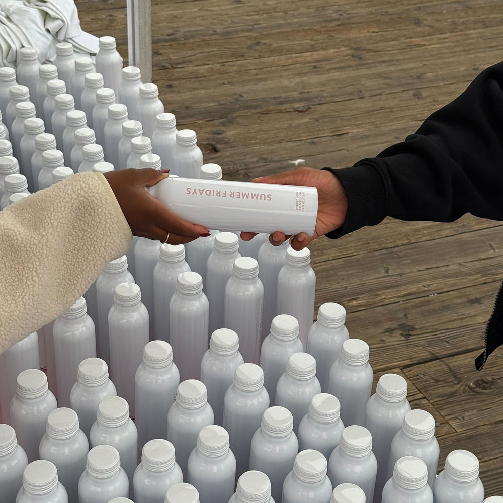 Two hands exchanging a white bottle labeled 'Silver River' among rows of similar bottles on a wooden surface.